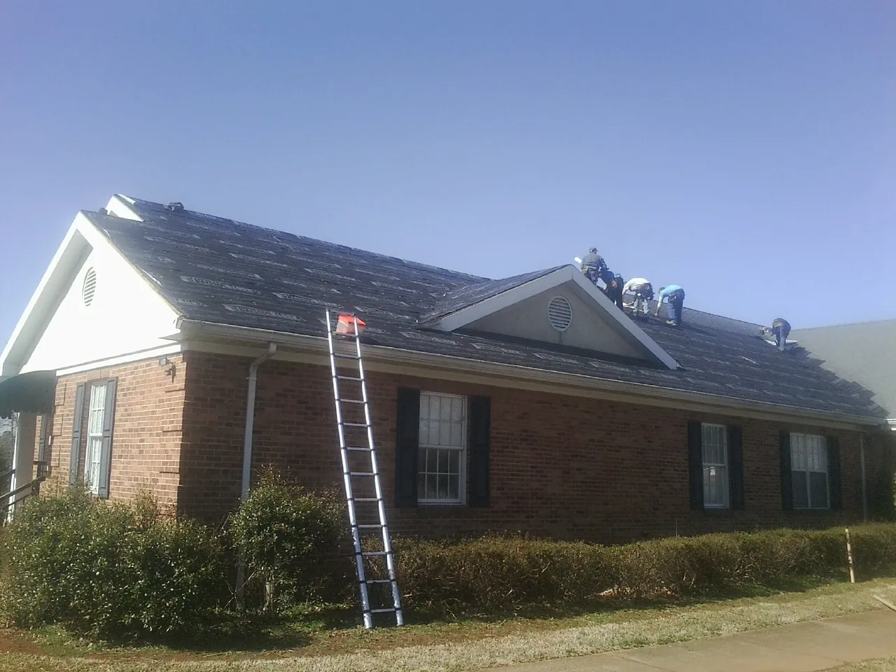 Crew tearing shingles off a brick ranch roof with a ladder set — Metal Roof Repair work by our crew in Sunderland