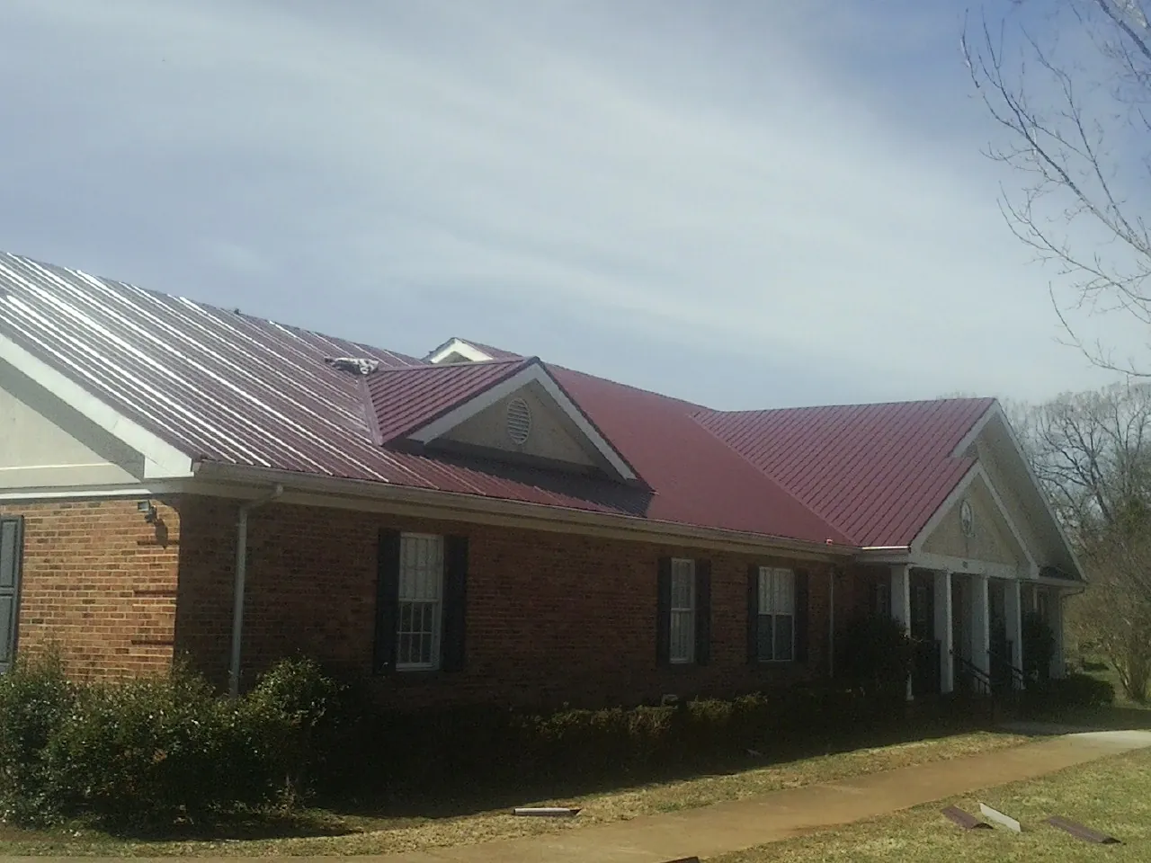 Red metal roof with gabled entries on a long brick building, from a Hail Damage Roof Repair job in Sunderland