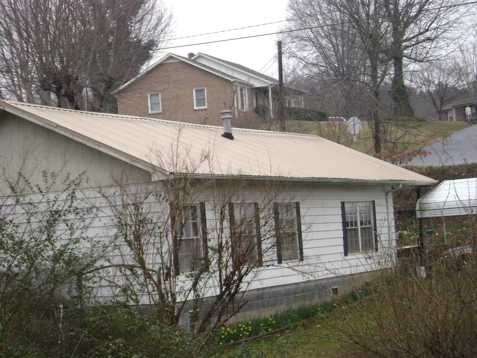 Tan metal roof on a white sided house set into a hillside — Commercial Roofing by Roofing Brothers in Sunderland